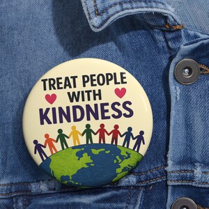May include: A round pinback button with a cream background featuring the text TREAT PEOPLE WITH KINDNESS in black letters, flanked by two red hearts. Below, a line of colorful stick figures holds hands over a blue and green globe illustration.