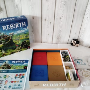 Könnte beinhalten: Das Brettspiel "Rebirth" wird gezeigt, mit einer Schachtel, die ein Schloss und den Spieltitel zeigt. Im Inneren der offenen Box befinden sich vier farbige Spielkomponentenhalter. Zusätzliche Komponenten und Spielbeutel sind ebenfalls sichtbar.