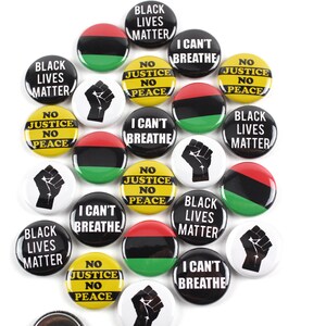May include: A collection of round buttons with various messages and designs. Some buttons feature the text "Black Lives Matter," "I Can't Breathe," and "No Justice No Peace." Other buttons display a raised fist graphic or the Pan-African flag colors.