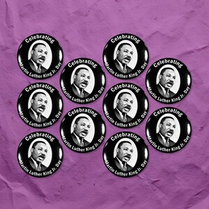 May include: A collection of black and white buttons featuring a portrait of Martin Luther King Jr. and the text "Celebrating Martin Luther King Jr. Day" in white lettering. The buttons are arranged on a purple textured background.