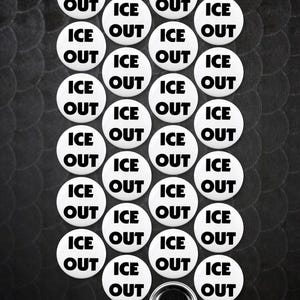 May include: A collection of white buttons with the words "ICE OUT" in black, arranged on a textured black background. One button is shown with a pin back. The buttons are circular and evenly spaced.