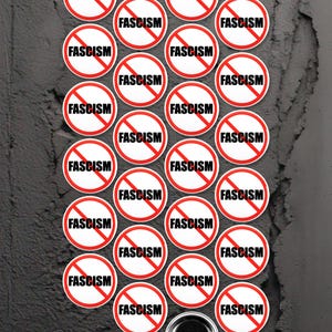Pode incluir: Uma coleção de 24 botões redondos vermelhos e brancos com a palavra "FASCISMO" impressa em letras pretas e uma linha vermelha diagonal que atravessa a palavra. Os botões estão dispostos em um padrão circular sobre uma superfície cinza texturizada.