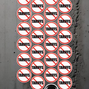 Könnte beinhalten: Eine Sammlung von 24 runden, weißen, roten und schwarzen Knöpfen mit dem Wort "TARIFFS" in schwarzen Buchstaben und einem roten diagonalen Strich durch das Wort. Die Knöpfe sind in einem Kreis auf einem grauen Betonuntergrund angeordnet.