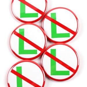 May include: A collection of five round, white buttons with a red border and a red diagonal line through a green letter "L". The buttons are arranged on a white background.