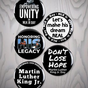 May include: A collection of five black and white buttons with text and images related to Martin Luther King Jr. The buttons feature phrases like "Empowering Unity," "Honoring His Legacy," and "Don't Lose Hope."