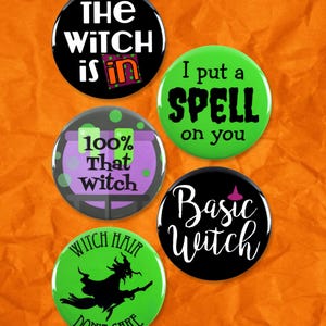 May include: A collection of round, colorful witch-themed buttons. The buttons feature phrases like "The Witch is In," "I put a SPELL on you," and "Basic Witch." Other buttons say "100% That Witch" and "Witch Hair Don't Care."