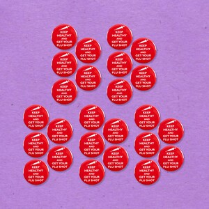Könnte beinhalten: Eine Ansammlung roter runder Aufkleber mit dem weißen Text "KEEP HEALTHY AND GET YOUR FLU SHOT". Die Aufkleber sind auf einem hellvioletten Hintergrund angeordnet. Die Aufkleber sind ein Produkt zur Gesundheitsförderung.