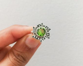 Pode incluir: Um anel de prata com uma gema verde engastada em um design floral.