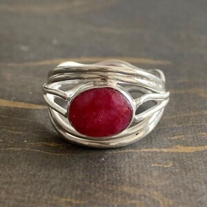 May include: A silver ring with a red gemstone set in a delicate, interwoven design.