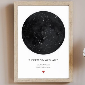 Puede incluir: Impresión enmarcada con un mapa estelar en blanco y negro, en un marco de madera clara. El texto "THE FIRST SKY WE SHARED" se muestra debajo del mapa, junto con la fecha y las coordenadas. Un pequeño corazón rojo está en la parte inferior.
