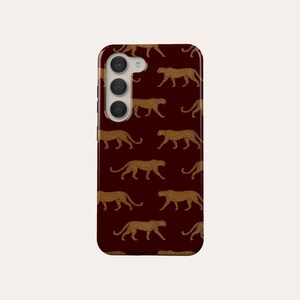 May include: A burgundy phone case with a repeating pattern of gold leopard silhouettes.