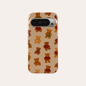 Könnte beinhalten: Eine Handyhülle mit einem sich wiederholenden Muster aus kleinen Teddybären in verschiedenen Posen und Outfits. Die Bären sind in Brauntönen gehalten und tragen rote, grüne und braune Outfits. Die Hülle hat einen beigefarbenen Hintergrund und einen Kameraausschnitt.