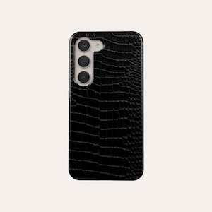 Peut inclure: Étui de téléphone noir avec un motif en peau de crocodile. L'étui a une bosse de caméra surélevée avec trois objectifs.
