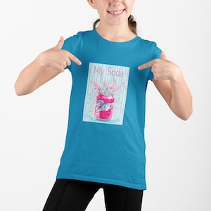 May include: A turquoise t-shirt with a graphic of a pink soda can, the word "Pop", and the text "My Soda". The soda can is shown with a splash of pink liquid. The shirt is being pointed at by a person.