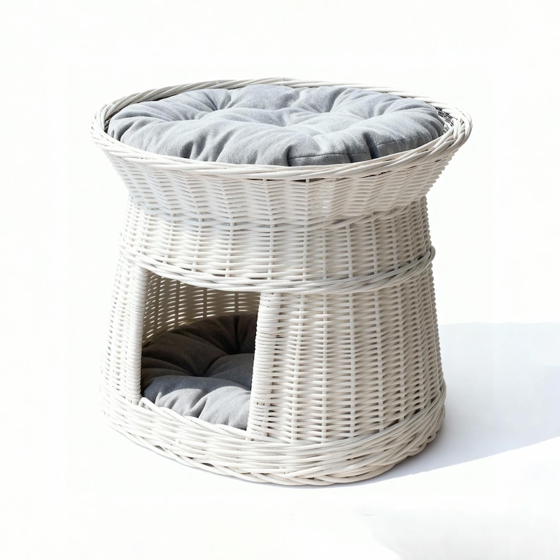 May include: A white wicker pet bed with a round top and a lower enclosed area. The bed has a gray cushion on top and inside the enclosed space. The woven design gives it a natural, airy look, suitable for cats or small dogs.