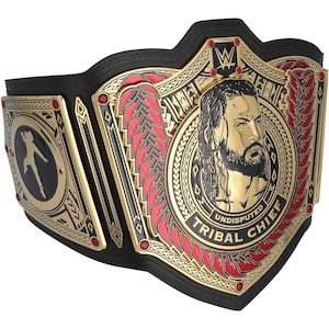 May include: A gold and black wrestling championship belt with red accents. The belt features a portrait of a man and the words "UNDISPUTED TRIBAL CHIEF". The belt has a black leather strap and gold detailing.