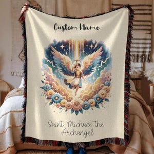 May include: Cream-colored woven throw blanket featuring an illustration of Saint Michael the Archangel. The design includes an angel with large wings, surrounded by flowers and clouds. The text "Custom Name" and "Saint Michael the Archangel" are also visible.