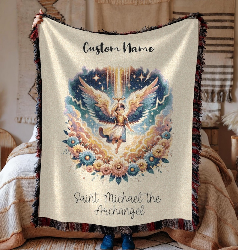 May include: Cream-colored woven throw blanket featuring an illustration of Saint Michael the Archangel. The design includes an angel with large wings, surrounded by flowers and clouds. The text "Custom Name" and "Saint Michael the Archangel" are also visible.