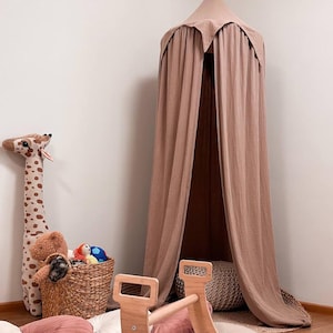 May include: A light brown fabric play tent with a pointed top, a wooden climbing frame, and a plush pink and cream cushion. The tent is set up in a room with a white wall and a giraffe stuffed animal.