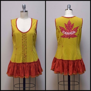 Op de afbeelding: Een gele, mouwloze jurk met een rode geruite zoom en een rood esdoornblad met het woord "CANADA" op de achterkant.