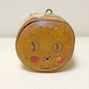 May include: A round wooden box with a painted face, featuring eyes, a nose, and a mouth. The box is labeled "Sally Tracy, Shipherd, Lincoln, Mich."