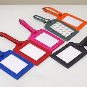 Può includere: Un set di cinque etichette per bagagli rettangolari in blu, rosso, rosa, verde scuro e arancione. Ogni etichetta presenta un cinturino regolabile abbinato con fibbia in metallo e una finestra in plastica trasparente. L'etichetta verde ha un'etichetta 3M.