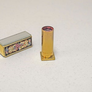 May include: A gold lipstick tube with a floral design on the case. The lipstick tube is empty and the case is closed.