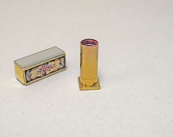 May include: A gold lipstick tube with a floral design on the case. The lipstick tube is empty and the case is closed.