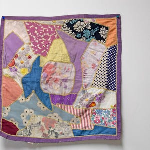 May include: A colorful patchwork quilt with a variety of floral, polka dot, and striped fabric pieces. The quilt features a blue star shape and is bordered with a purple fabric and gold stitching.