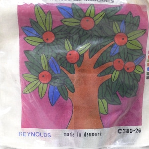 May include: A needlepoint canvas with a vibrant tree design, showcasing red fruit, green and blue leaves, and an orange trunk set against a pink backdrop. The canvas is packaged in a clear plastic bag. The text "REYNOLDS made in denmark" is visible.