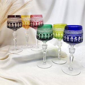 Puede incluir: Un juego de seis copas de vino de cristal en colores morado oscuro, amarillo, rosa, verde, verde lima y azul. Cada copa presenta un tallo transparente con un nudo texturizado, un patrón de diamante en la parte superior y estrías verticales.
