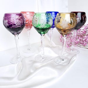 Könnte beinhalten: Sechs Weingläser mit Stiel und aufwendigen Schliffmustern. Die Gläser sind in verschiedenen Farben, darunter lila, rosa, grün, blau, bernsteinfarben und rot.