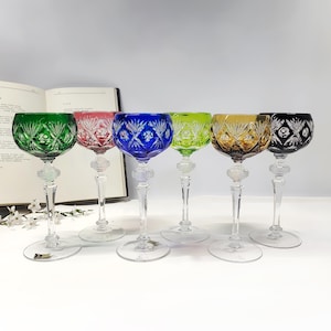 Puede incluir: Seis copas de vino de cristal de colores con intrincados patrones tallados. Las copas presentan una variedad de colores, incluyendo verde, rosa, azul, amarillo y negro. Cada copa tiene un tallo y una base transparentes, y están dispuestas en fila.