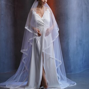 Two tier wedding veil made of soft Italian tulle with velvet ribbon edge hand trimmed with pearls. Long layered cathedral veil in ivory, designed for modern brides who want a classic look with subtle pearl details. This bridal veil with pearl trim is perfect for weddings in any season, including Christmas ceremonies and New Year celebrations, adding timeless style to bridal portraits and the walk down the aisle.
