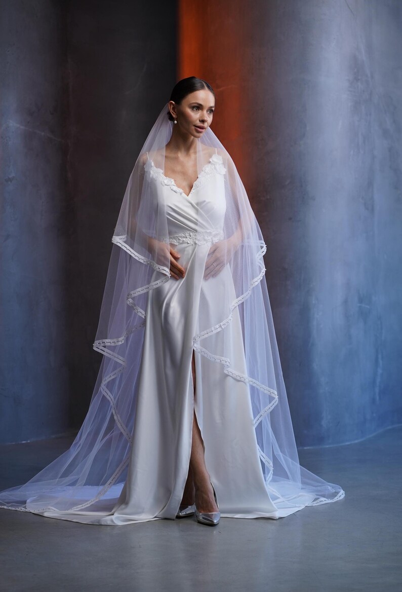 Two tier wedding veil made of soft Italian tulle with velvet ribbon edge hand trimmed with pearls. Long layered cathedral veil in ivory, designed for modern brides who want a classic look with subtle pearl details. This bridal veil with pearl trim is perfect for weddings in any season, including Christmas ceremonies and New Year celebrations, adding timeless style to bridal portraits and the walk down the aisle.