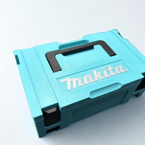 Puede incluir: Un malet&iacute;n de almacenamiento rectangular de pl&aacute;stico azul claro con un asa de transporte negra y cierres de esquina negros. La marca Makita est&aacute; grabada en letras blancas en la parte superior de la tapa, que tiene un dise&ntilde;o moldeado.