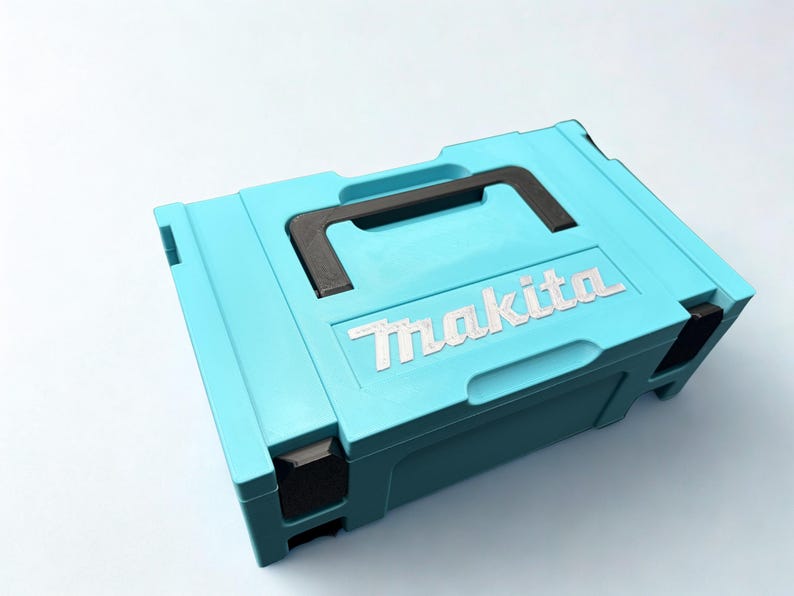 Puede incluir: Un malet&iacute;n de almacenamiento rectangular de pl&aacute;stico azul claro con un asa de transporte negra y cierres de esquina negros. La marca Makita est&aacute; grabada en letras blancas en la parte superior de la tapa, que tiene un dise&ntilde;o moldeado.