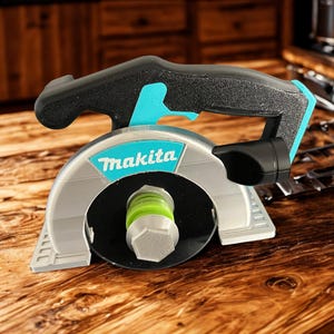 Puede incluir: Una r&eacute;plica de herramienta de sierra circular de la marca Makita con carcasa plateada, mango negro con detalles en turquesa y una zona central de hoja circular negra con un perno hexagonal de color verde lima y plata, con textura en capas.
