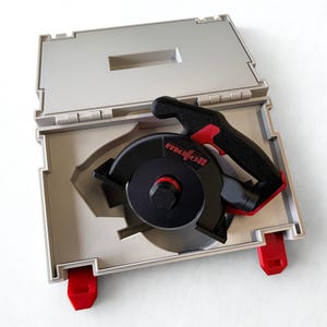 Puede incluir: Un accesorio de herramienta el&eacute;ctrica Mafell en negro y rojo con una carcasa circular y un mango, guardado dentro de un malet&iacute;n de transporte de pl&aacute;stico gris claro. El malet&iacute;n cuenta con cierres rojos y un interior moldeado para el equipo.