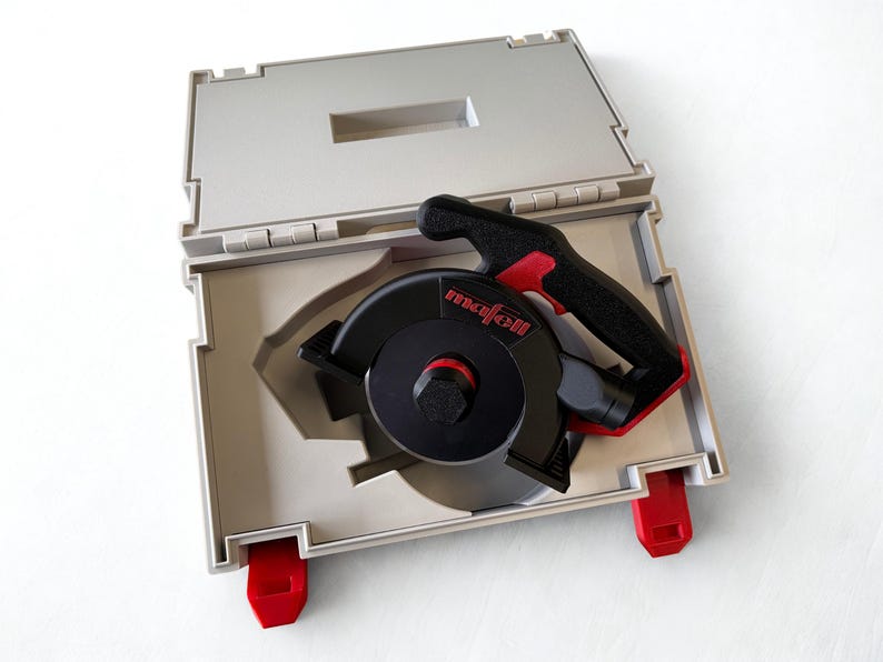 Puede incluir: Un accesorio de herramienta el&eacute;ctrica Mafell en negro y rojo con una carcasa circular y un mango, guardado dentro de un malet&iacute;n de transporte de pl&aacute;stico gris claro. El malet&iacute;n cuenta con cierres rojos y un interior moldeado para el equipo.