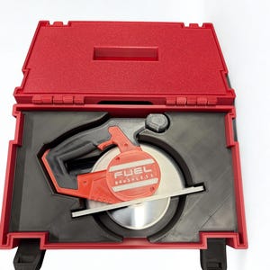 Puede incluir: Una sierra circular roja y negra con la etiqueta FUEL BRUSHLESS en el lateral, colocada dentro de un inserto negro a medida en un malet&iacute;n de transporte de pl&aacute;stico rojo. La sierra cuenta con una hoja met&aacute;lica y un mango integrado.