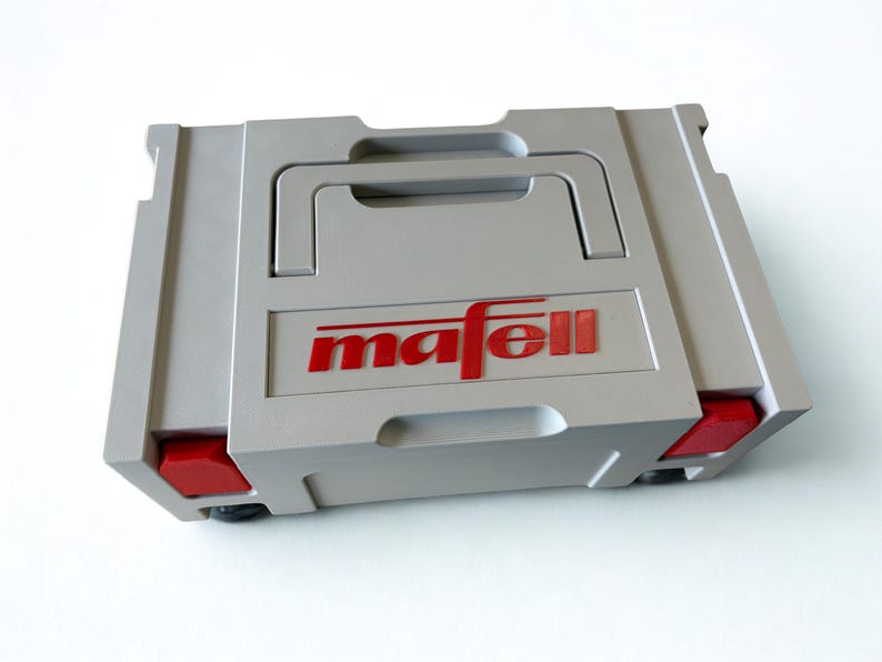 Puede incluir: Un malet&iacute;n de transporte rectangular de pl&aacute;stico gris claro con un asa superior y cierres rojos en los laterales. El nombre de la marca mafell est&aacute; impreso en letras rojas en el centro de la parte frontal. El malet&iacute;n presenta un dise&ntilde;o estructurado.