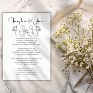 May include: A white card with the text "For my beautiful Auntie" and a poem. The card features line art illustrations of two women and floral accents. A bouquet of white flowers rests on the right.