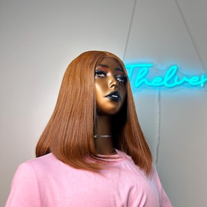 May include: A mannequin wearing a pink t-shirt and a straight, shoulder-length auburn wig.