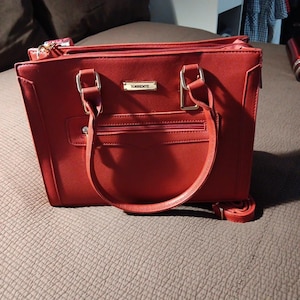 K&ouml;nnte beinhalten: Eine rote Ledertasche mit goldenen Beschl&auml;gen und dem Wort "Torrente" auf der Vorderseite.