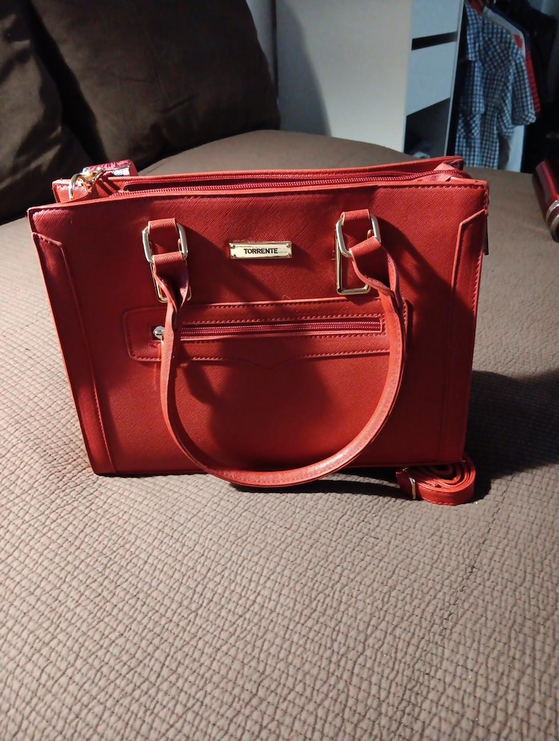 K&ouml;nnte beinhalten: Eine rote Ledertasche mit goldenen Beschl&auml;gen und dem Wort "Torrente" auf der Vorderseite.