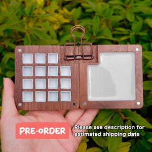 Puede incluir: Paleta de acuarela de madera con un clip color cobre, con 16 pocillos blancos y una gran zona de mezcla. El texto "PRE-ORDER" es visible. El texto "Please see description for estimated shipping date" también es visible.