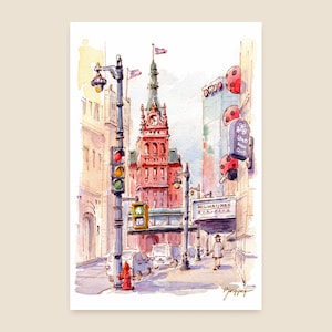 Könnte beinhalten: Aquarellmalerei einer Stadtstraßenszene. Ein hohes rotes Backsteingebäude mit einem Uhrturm ist der Mittelpunkt. Straßenlaternen, Ampeln und ein Schild mit der Aufschrift "Milwaukee Building" sind sichtbar. Eine Person geht auf dem Bürgersteig.