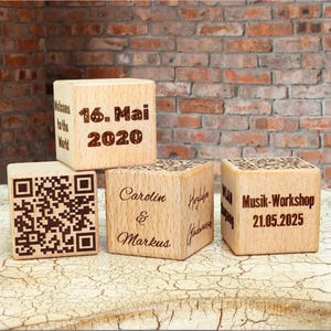 Puede incluir: Cuatro bloques de madera con texto grabado. El primer bloque dice "16. Mai 2020", el segundo bloque tiene un código QR, el tercer bloque dice "Carolin & Markus", y el cuarto bloque dice "Musik-Workshop 21.05.2025".