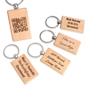 Könnte beinhalten: Fünf Schlüsselanhänger aus Holz mit verschiedenen gravierten Texten und einem QR-Code. Die Schlüsselanhänger sind hellbraun und haben einen silbernen Metallring.